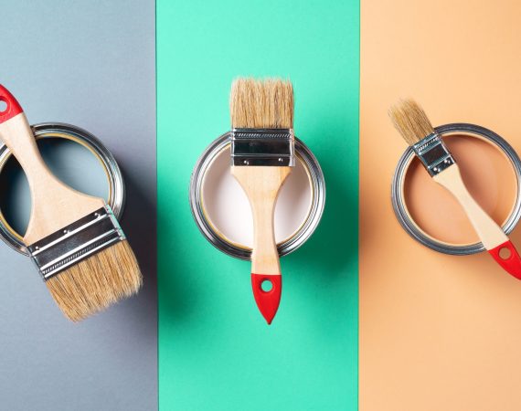 Metal paint cans and paint brushes on multicolor background. Top view. Copy space. Trendy green